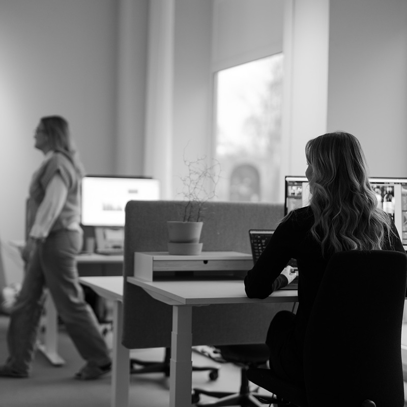 Kvinna som sitter framför datorn, i bakgrunden rör sig en kollega