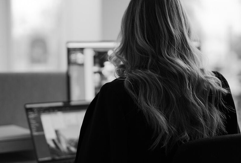 kvinna som sitter med ryggen vänd mot kameran och jobbar på en dator