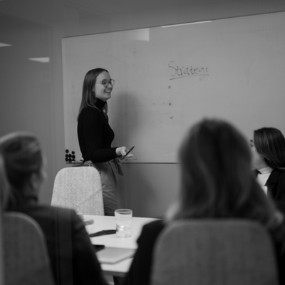 Kvinna som står framför whiteboard och presenterar framför tre andra personer